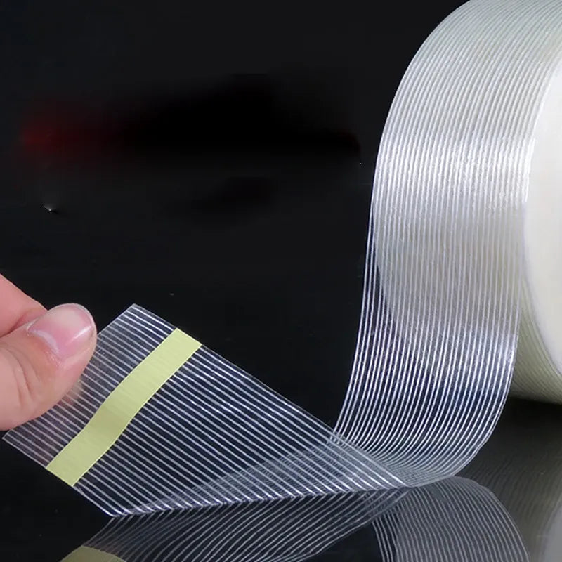 Hand pulling clear strip of cross-fiber filament tape with blue stripes from roll