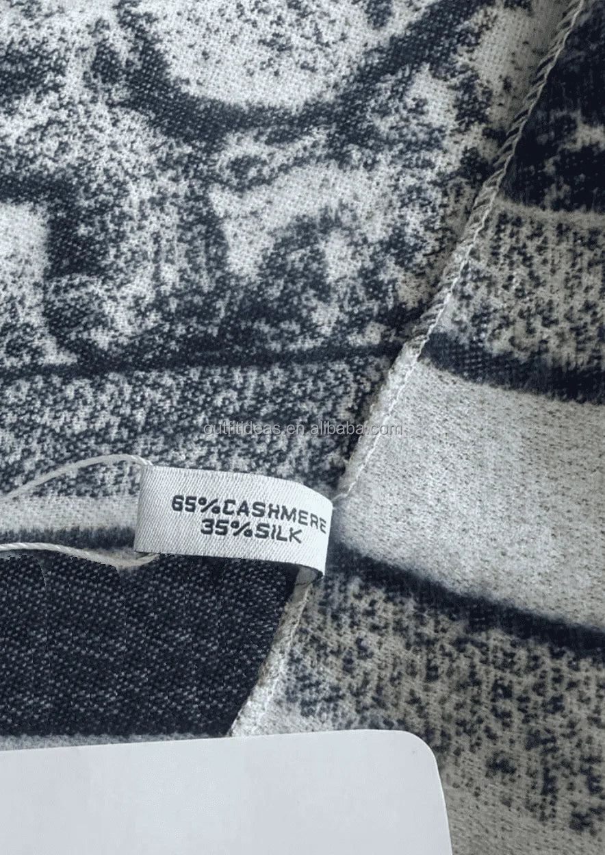 Luxury cashmere and silk scarf with black and white abstract textured print and branded material composition tag.