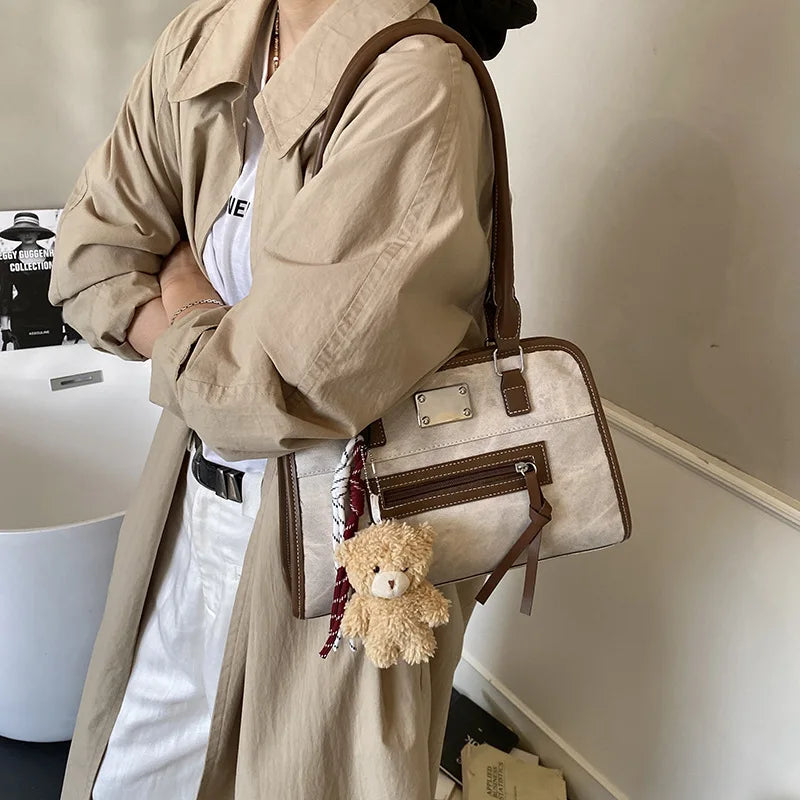Beige and brown soft leather trunk tote bag with front zip pocket, shoulder strap, and cute bear charm accessory.