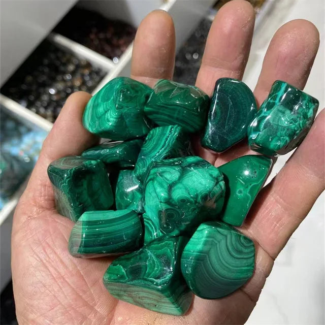 Green malachite tumbled stones in a hand, glossy with layered band patterns