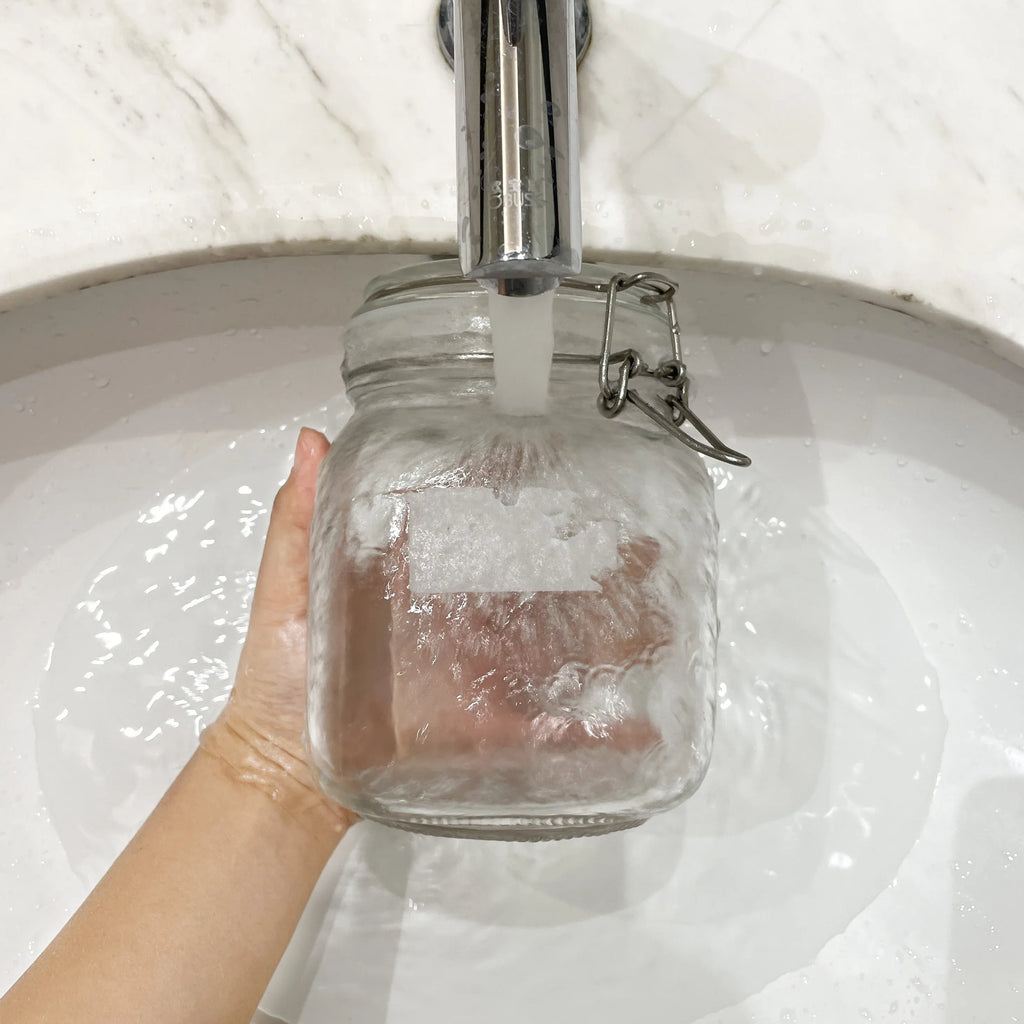 Hand applying a white blank water-soluble label sticker to a glass jar