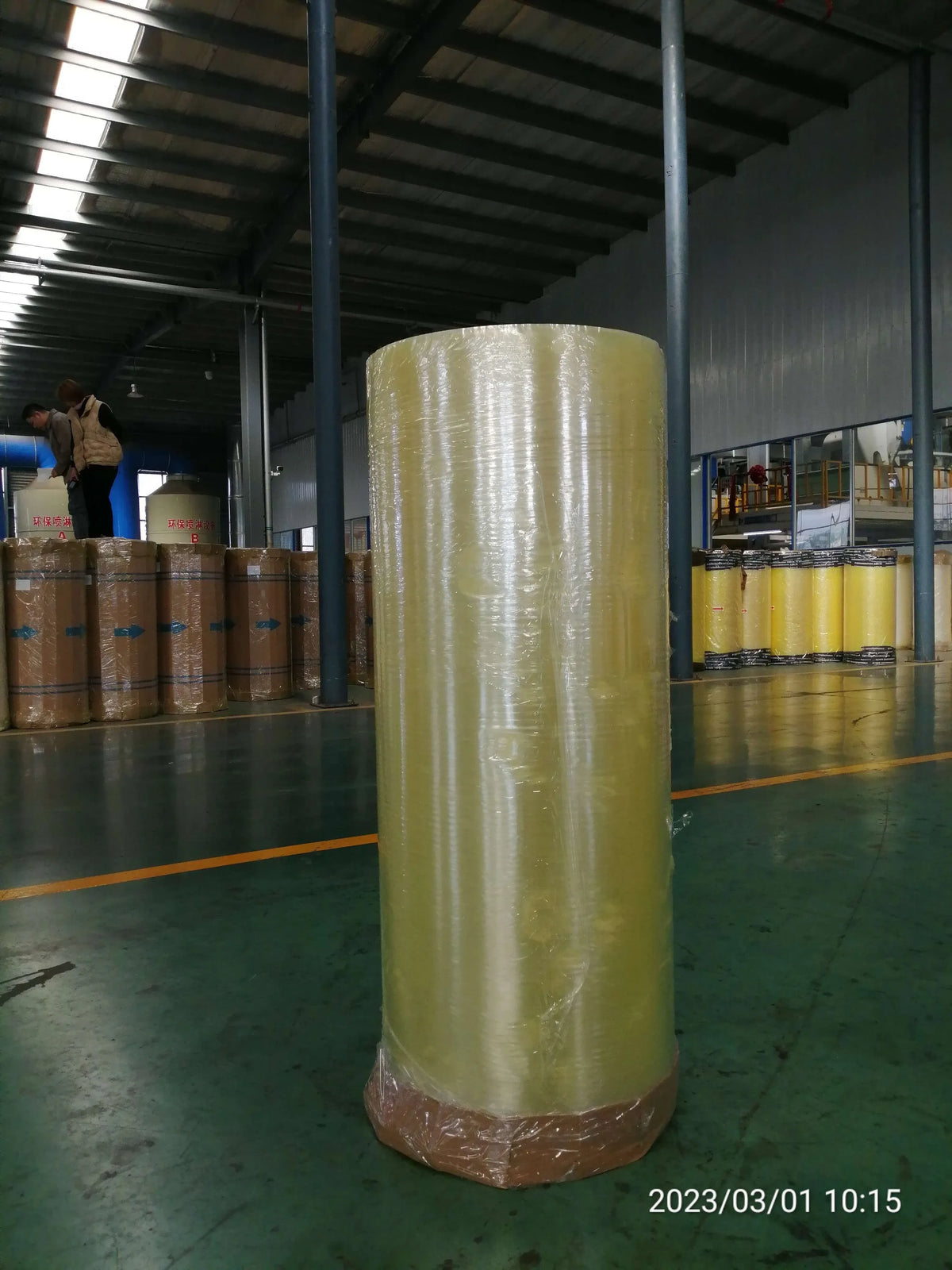 BOPP adhesive tape jumbo roll, tall pale yellow roll wrapped on base in warehouse