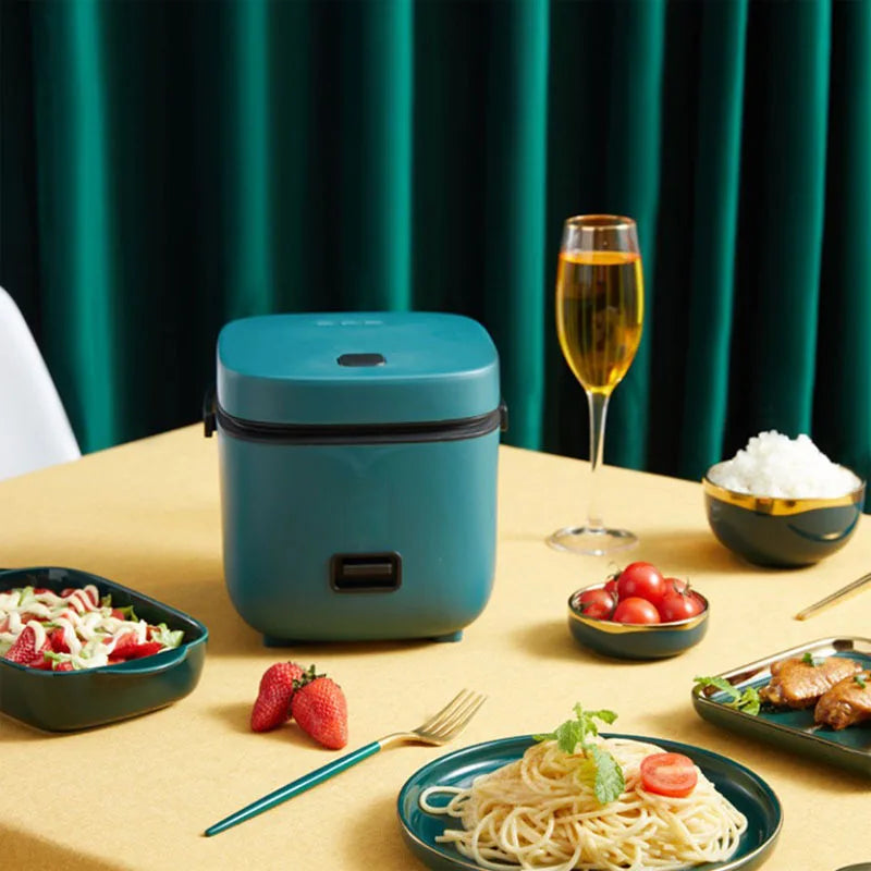 Teal mini rice cooker for warm meals on tabletop with spaghetti and side dishes