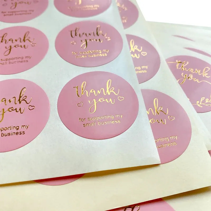 Close-up of pink round thank you stickers with gold-foil lettering and wreath