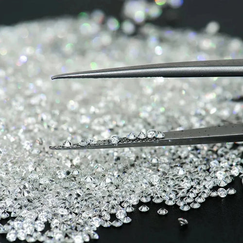 Loose round brilliant lab-grown diamonds scattered, shown with metal tweezers