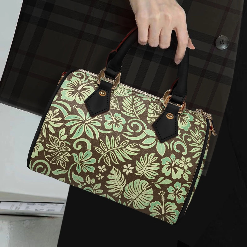 Pillow-style handbag in brown with light green tropical floral print, black leather handles, and gold hardware.
