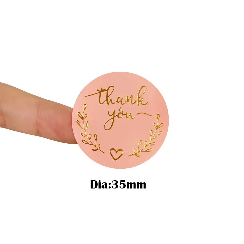 Pink round thank you sticker held up, gold wreath and heart; Dia:35mm