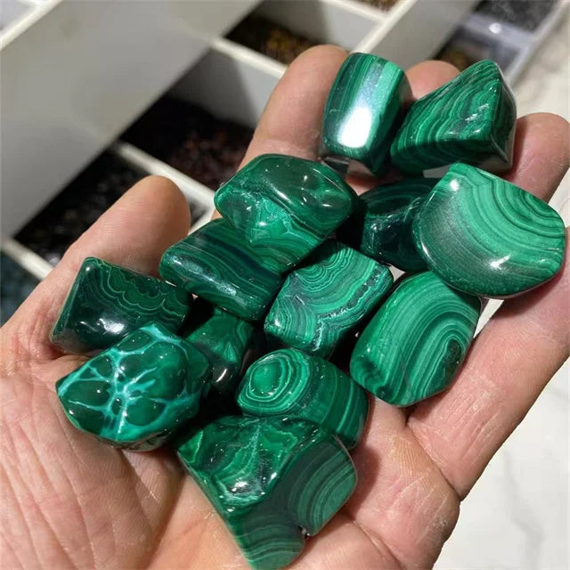Green malachite tumbled stones with smooth facets and wavy striations in hand