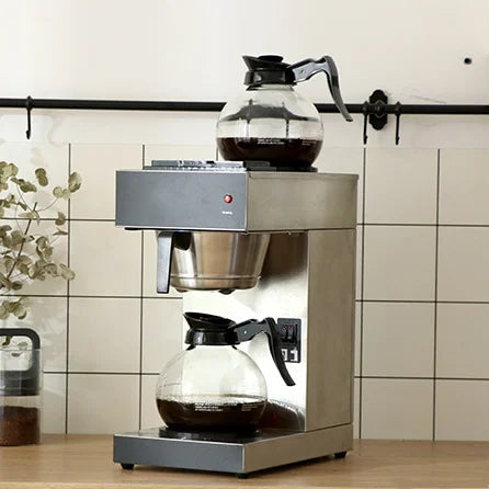 Commercial stainless steel coffee maker with two glass carafes on a kitchen counter.