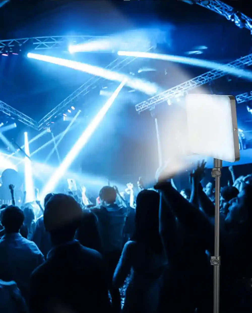 Square LED video light panel on an adjustable stand, emitting bright white light in a dark concert venue setting.
