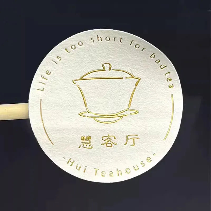 White round sticker label with gold teahouse pot logo and lettering, embossed.