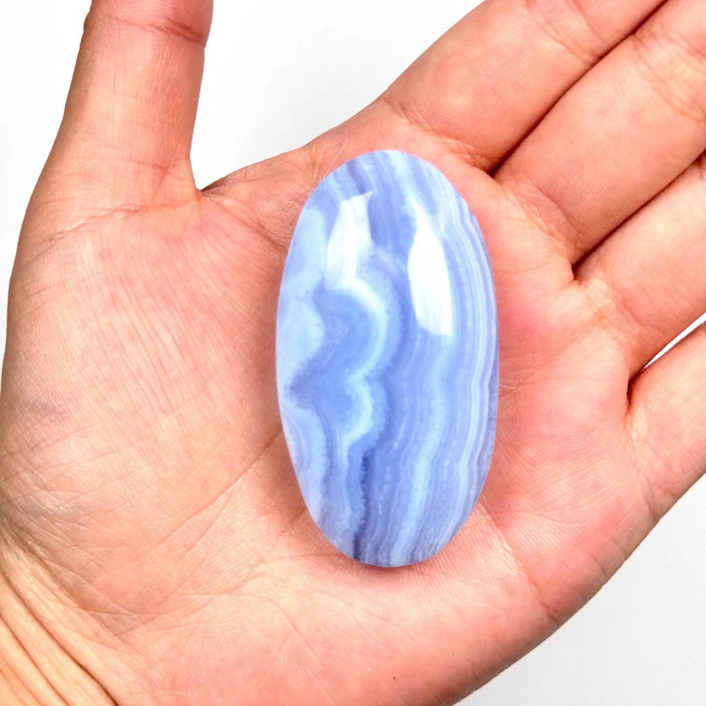 Blue lace agate palm stone resting in an open hand, smooth oval with wavy blue banding