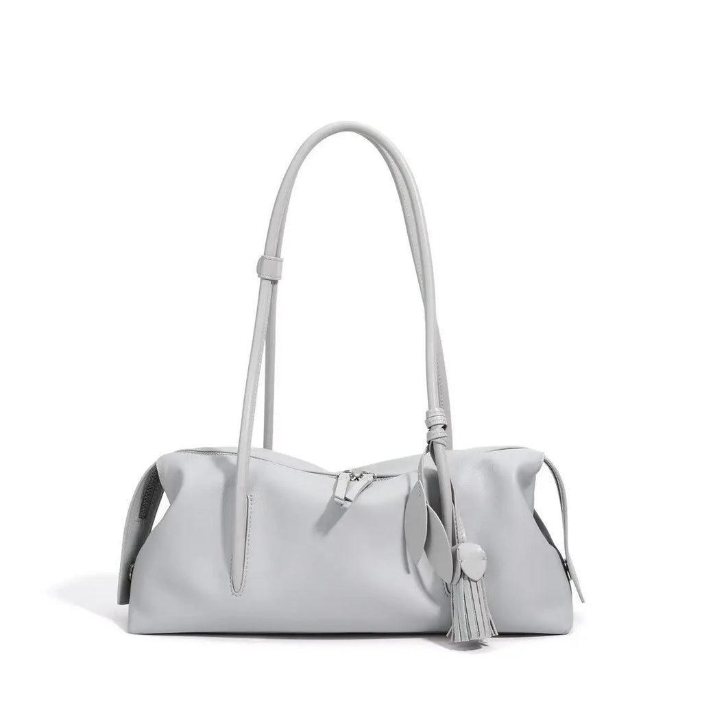 Light gray genuine leather trunk shoulder bag with tassel charm, top zipper closure, and soft cowhide construction.