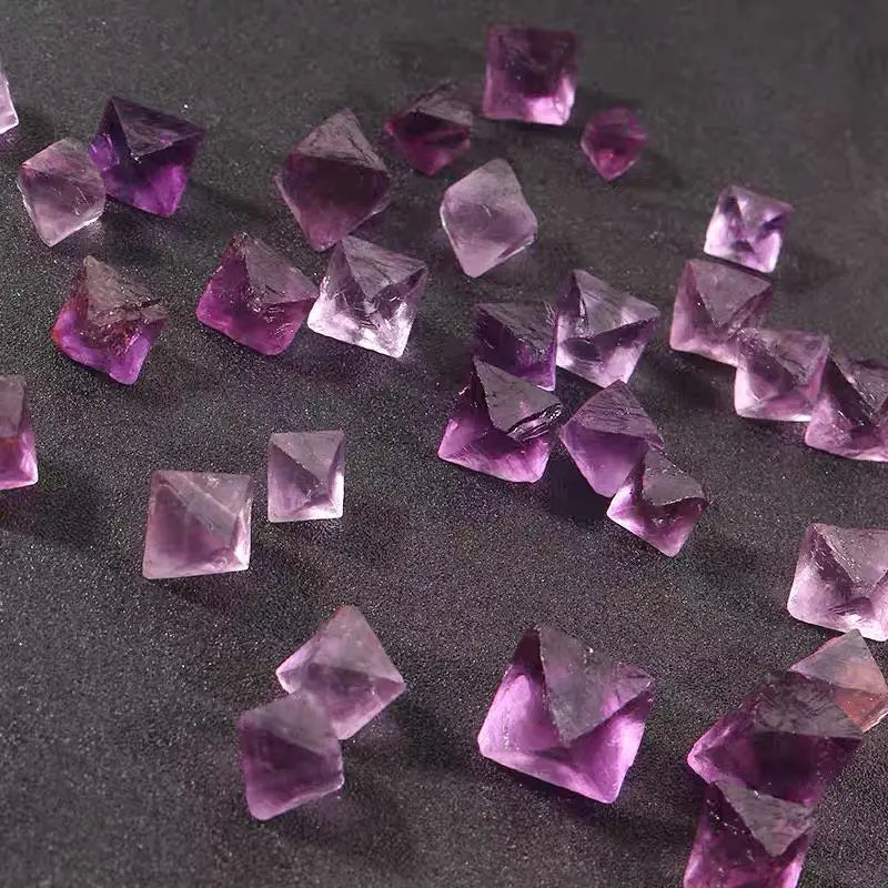 Purple rough crystal octahedra scattered in rows, faceted surfaces reflecting light