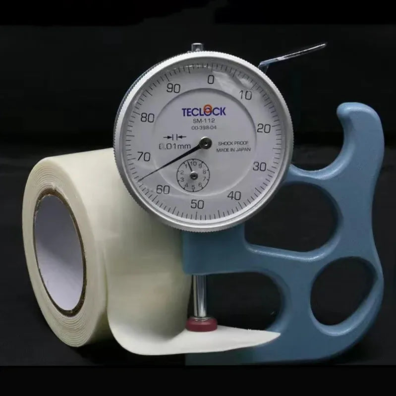 White double-sided foam mounting tape roll beside a measurement gauge