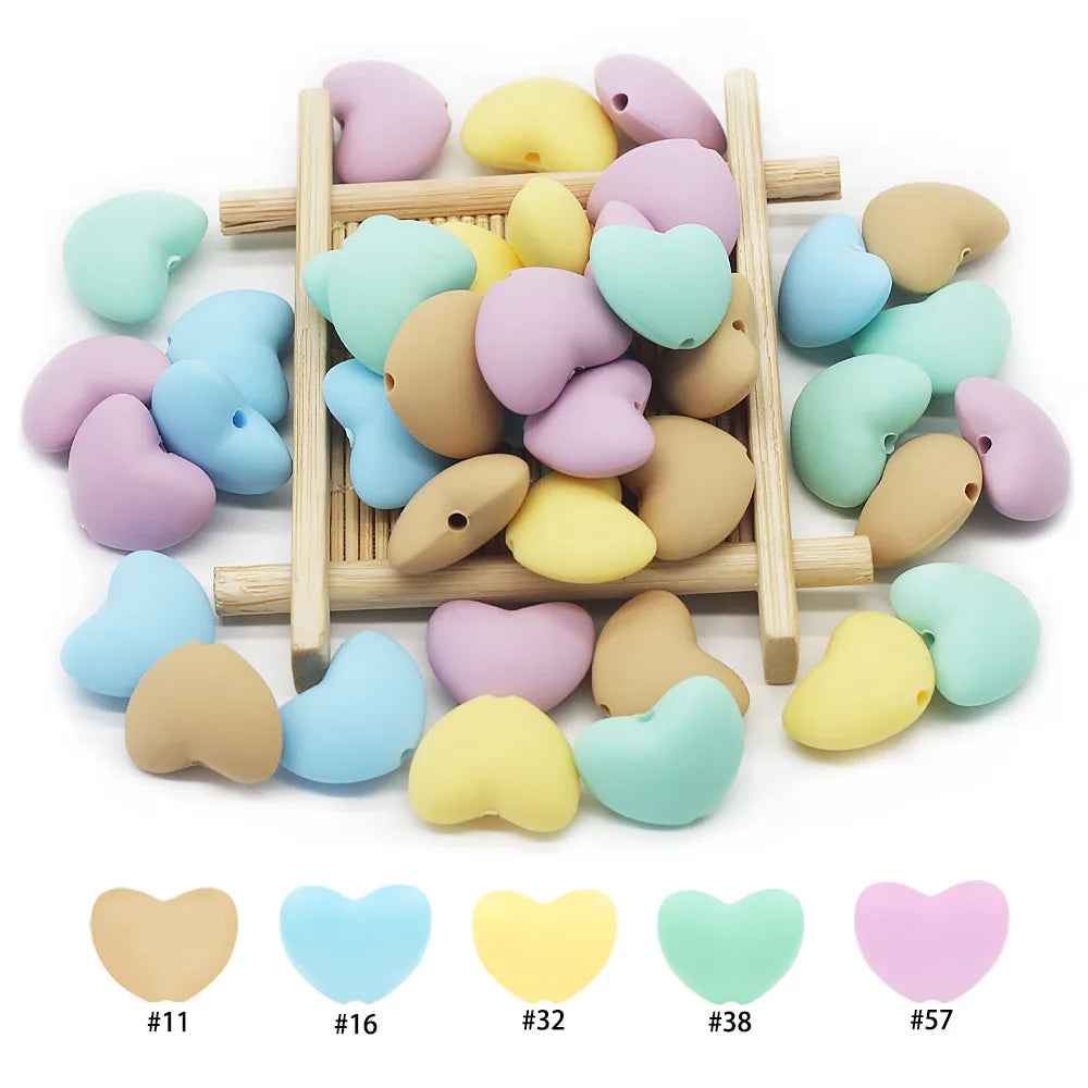 Multi-colored silicone heart beads for baby teething toys, available in pastel yellow, blue, pink, and tan.