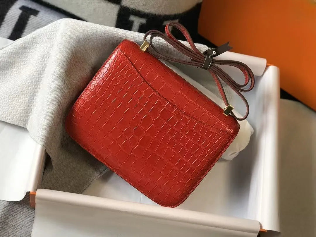 Red alligator-pattern leather compact shoulder bag with gold hardware, presented in a branded gift box.