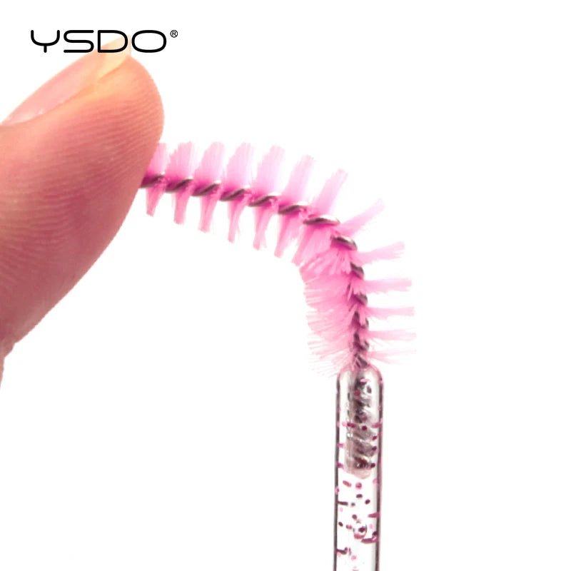 Flexible pink nylon lash spoolie brush with a clear plastic handle, used for grooming eyelashes and eyebrows.