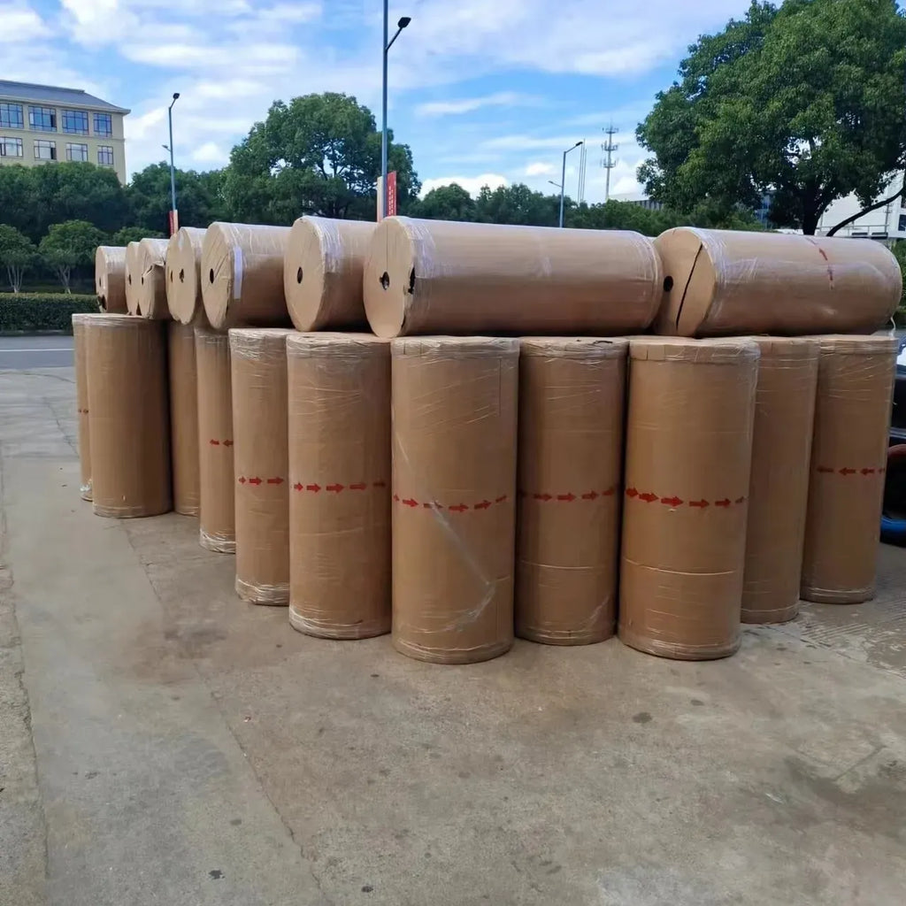 Stack of tan masking tape jumbo rolls with red bands on outdoor ground
