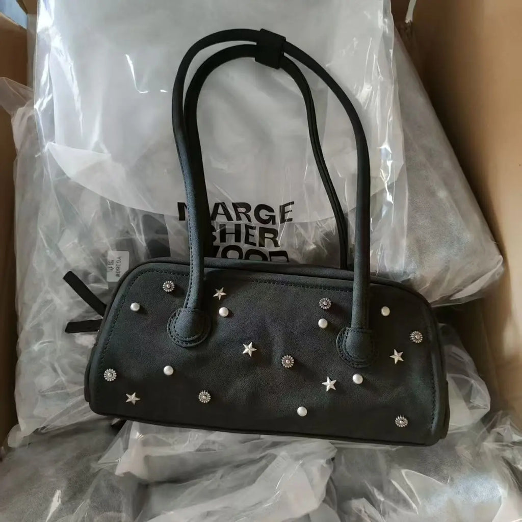 Black faux leather trunk-style shoulder tote with star and pearl studs, two handles, and top zip closure.
