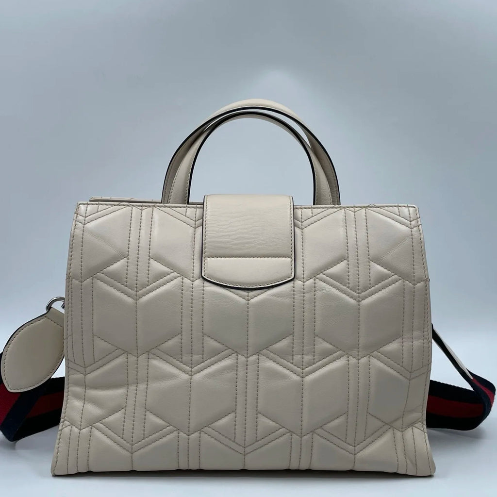 Off-white quilted leather designer tote bag with geometric stitching, top handles, and red-blue striped shoulder strap.