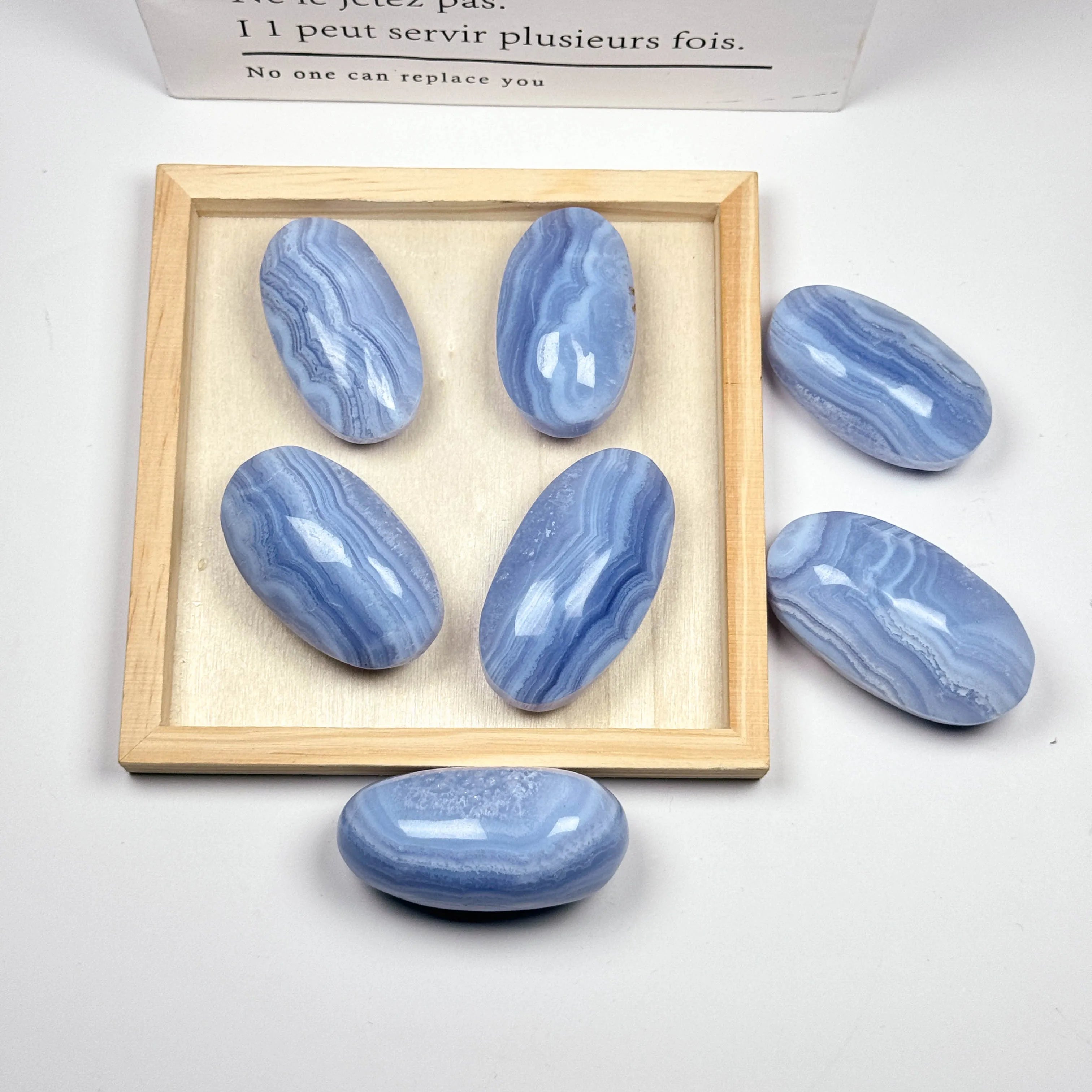 Blue lace agate palm stones in a wooden tray, smooth oval tumbled shapes with blue bands