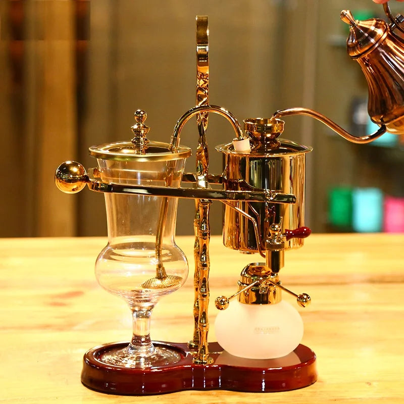 Luxury gold and glass Belgian balance coffee syphon maker on a dark wood base for elegant manual brewing.