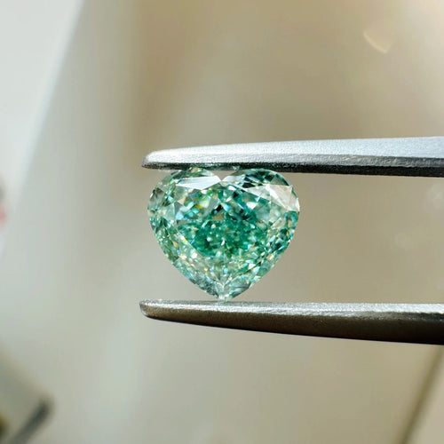 Heart-cut lab diamond in teal-green, viewed from the side between tweezers