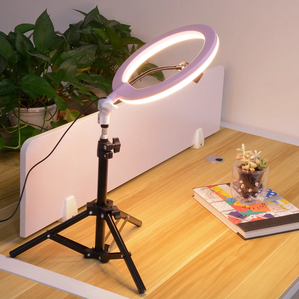 Light pink ring light on a black adjustable tripod stand for desk photography and video lighting.