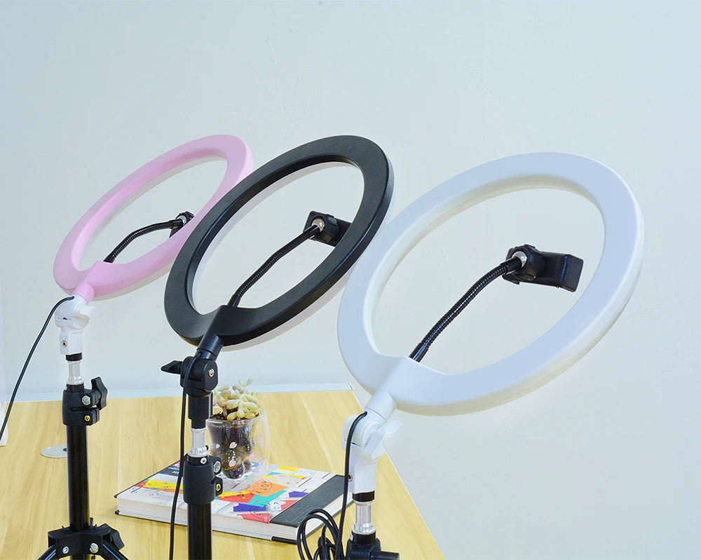 Three circular ring lights in pink, black, and white on adjustable stands with phone holders for photography or video.