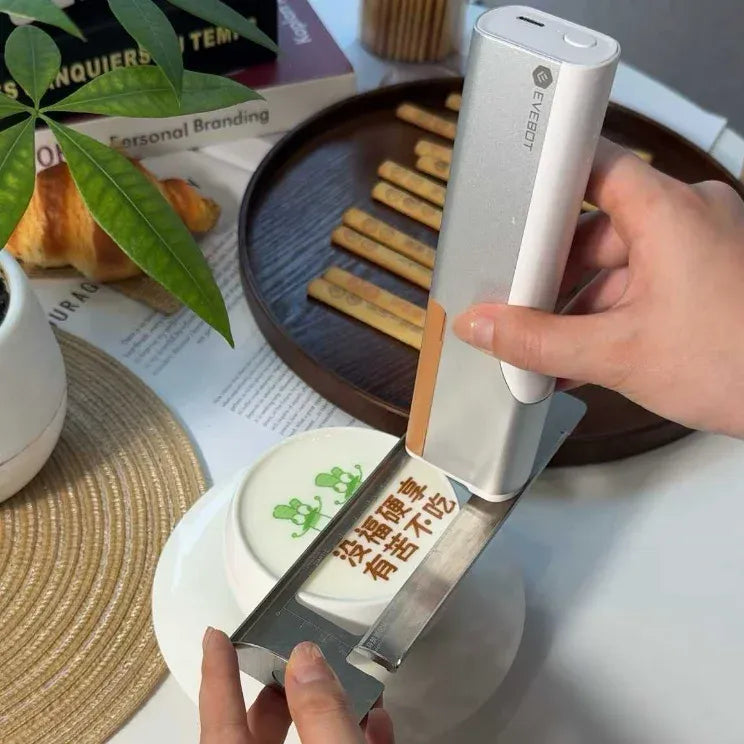 Handheld inkjet coffee printer dispensing over a small plate with text graphic