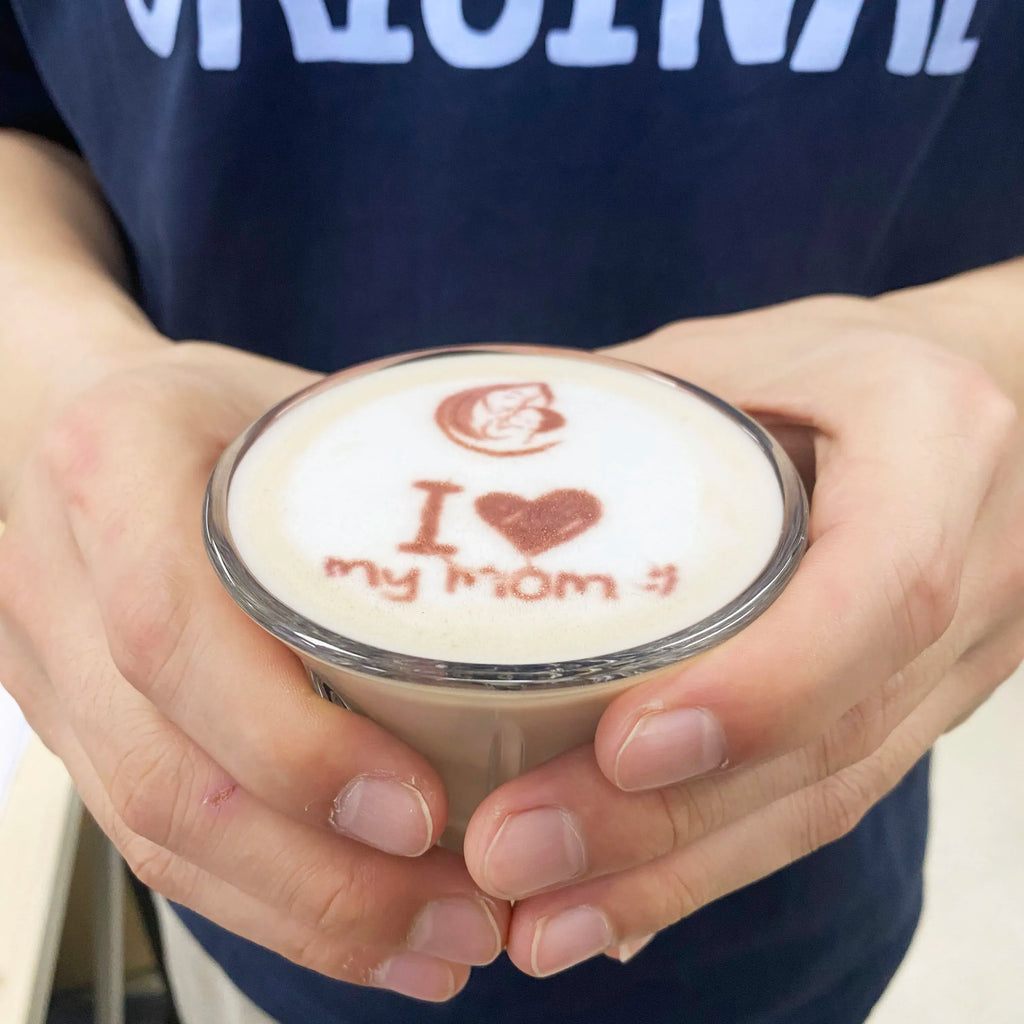 Handheld edible inkjet printer holding a round edible print reading “I heart my mom”.