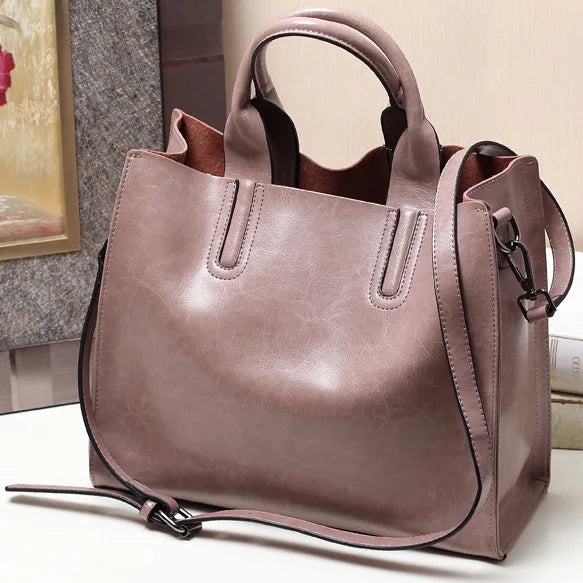 Mauve genuine leather handbag with double handles, adjustable shoulder strap, and minimalist luxury trunk style design.
