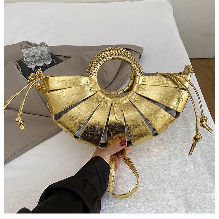 Metallic gold half-moon trunk bag with round braided handle, hollow-out design, and crossbody shoulder strap.