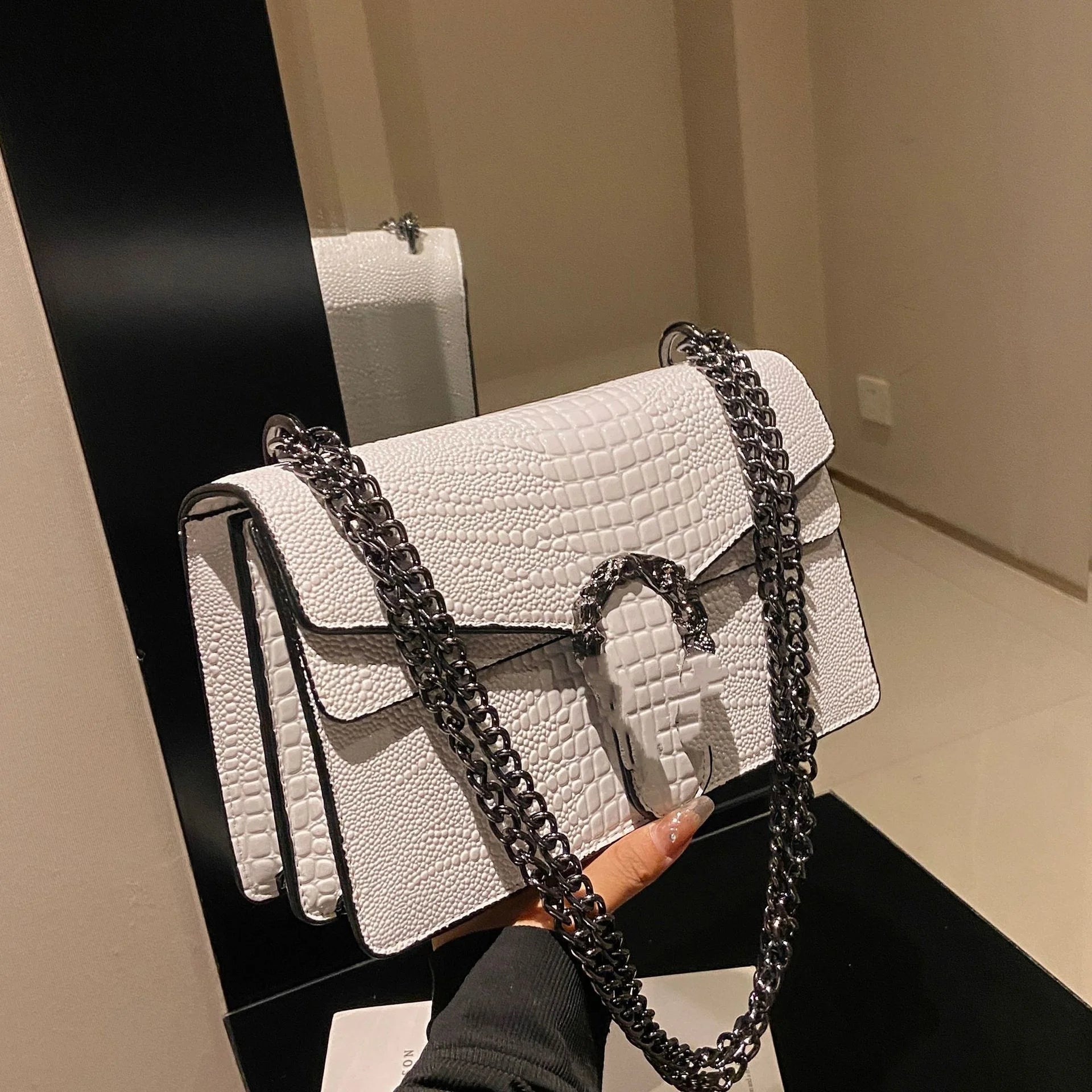 White luxury crocodile-pattern trunk crossbody bag with dark metallic chain strap and ornamental metal clasp closure.