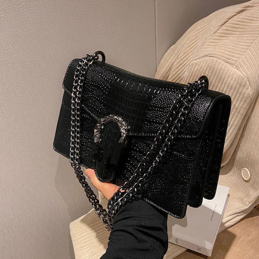 Black crocodile-embossed leather luxury crossbody bag with silver chain strap and ornate metal buckle clasp.