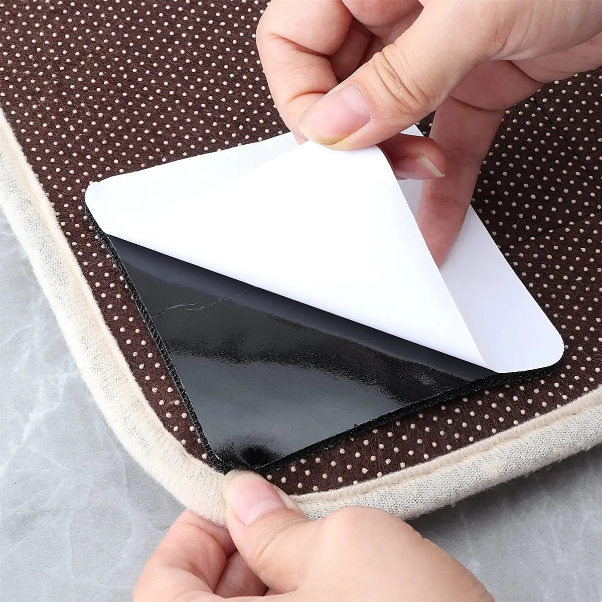 Double-sided carpet grip pad being pressed under a rug corner with black adhesive