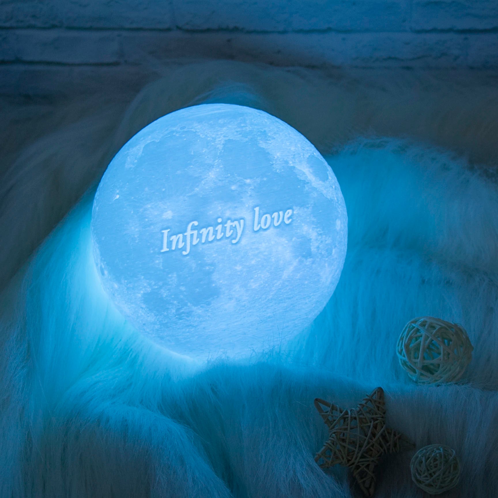 Blue moon lamp with the text "Infinity love" engraved, emitting a soft glow on a textured white surface.