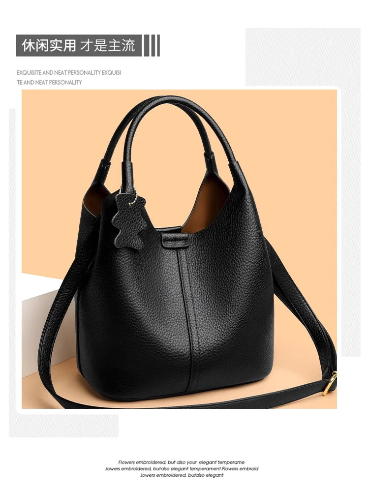 Black pebbled leather bucket handbag with top handles, adjustable crossbody strap, and cute bear charm. Casual style.