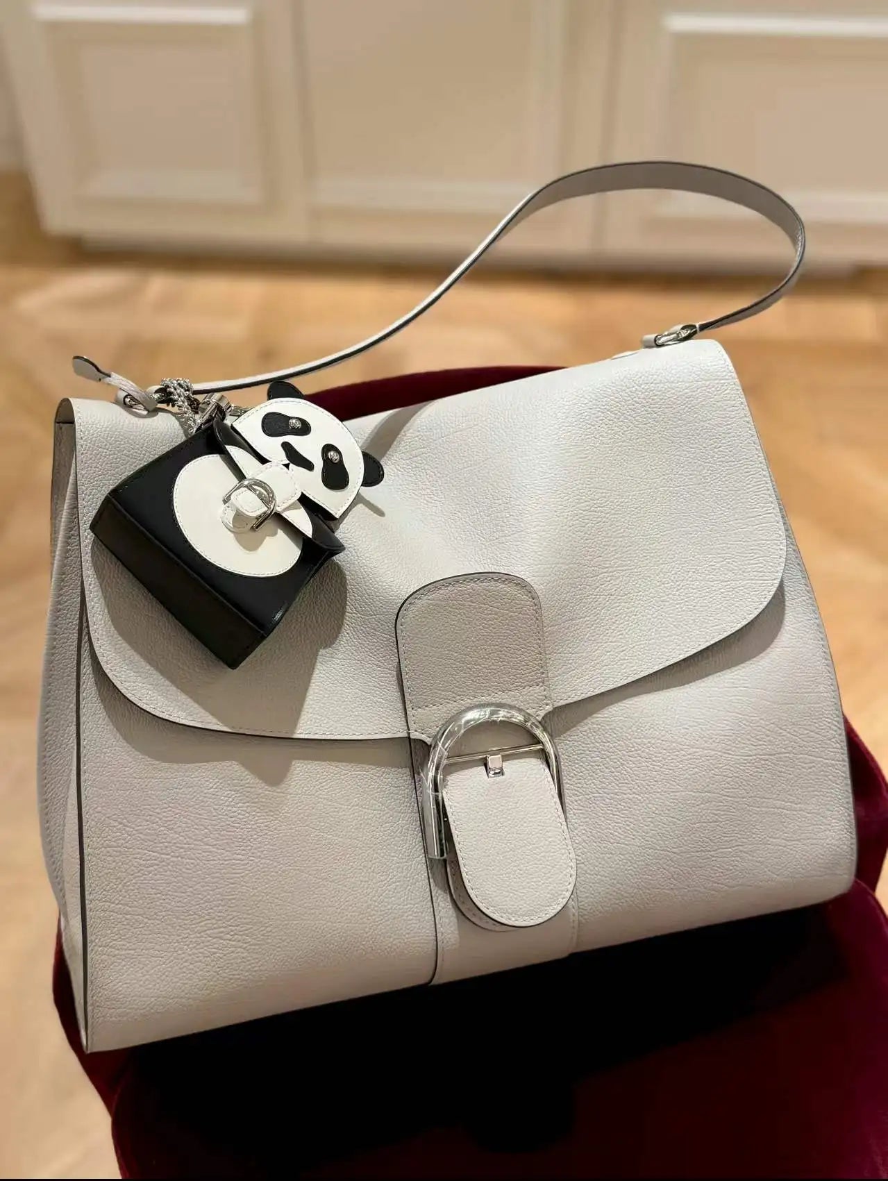 White pebble leather designer handbag with silver buckle closure and decorative panda charm shoulder bag accessory.