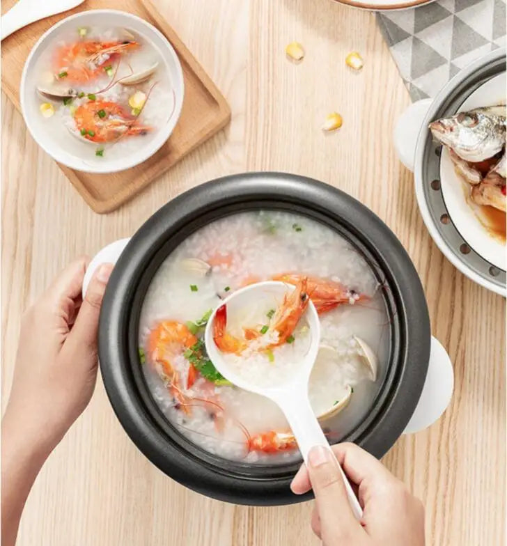 Mini electric rice cooker with open lid, black inner pot, hands stirring food with a spoon