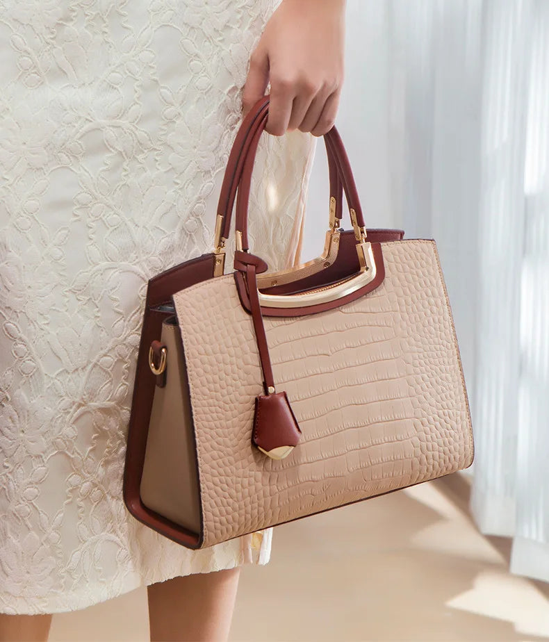 Beige and brown crocodile-textured tote bag with gold metal trim, top handles, and hanging charm. Fashion handbag.
