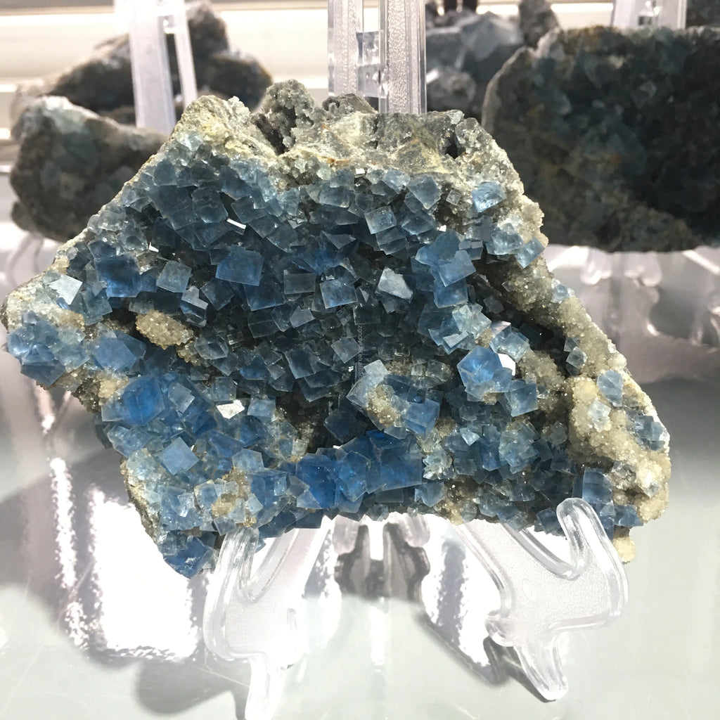 Blue fluorite crystal cluster on clear stand with rough stone matrix