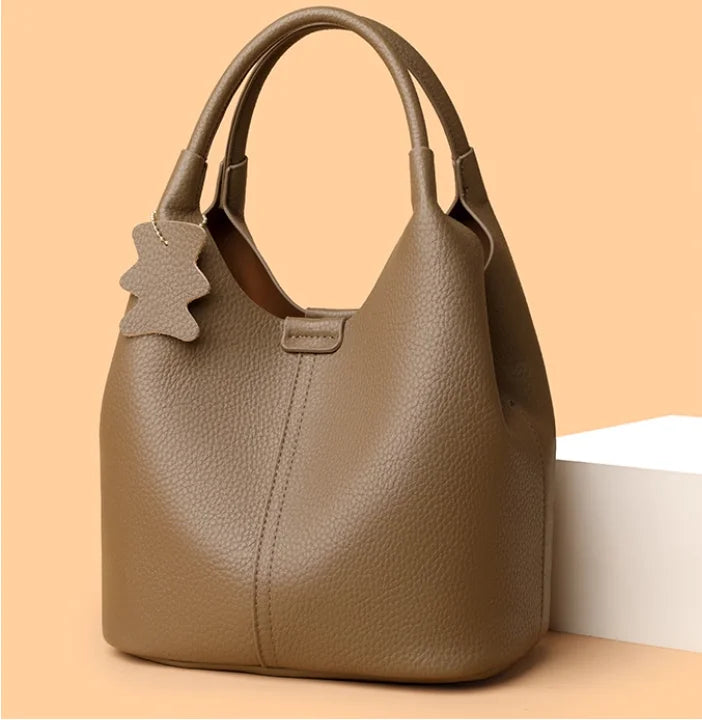 Taupe pebble leather bucket bag with top handles and a cute bear-shaped bag charm, ideal for casual commuting.