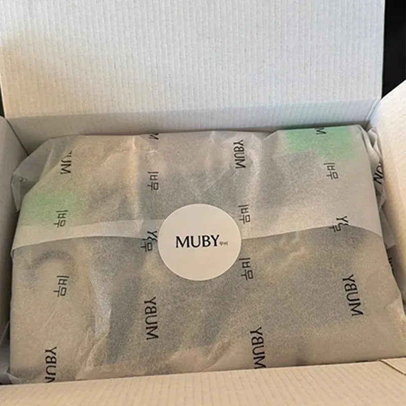 Round white and dark MUBY logo stickers inside a cardboard shipping box