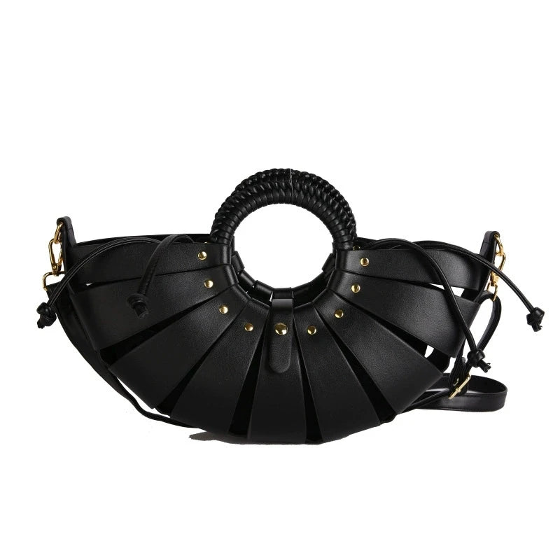 Black half-moon trunk handbag with hollow-out slats, round braided handle, and gold stud accents. Crossbody style.