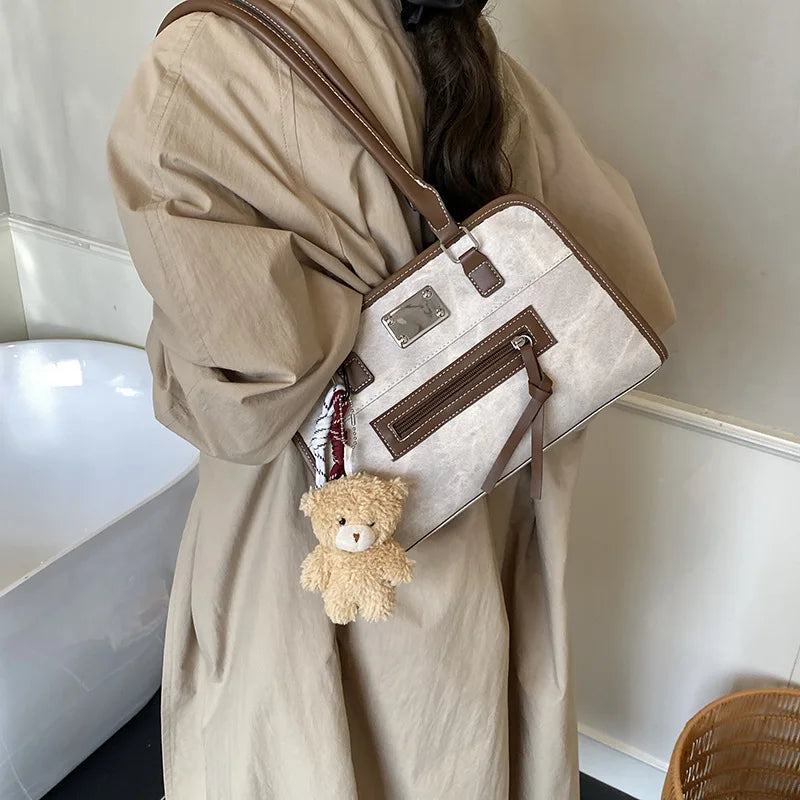 Beige soft leather trunk tote with brown trim, zipper pocket, metal plaque, and cute teddy bear charm shoulder bag.