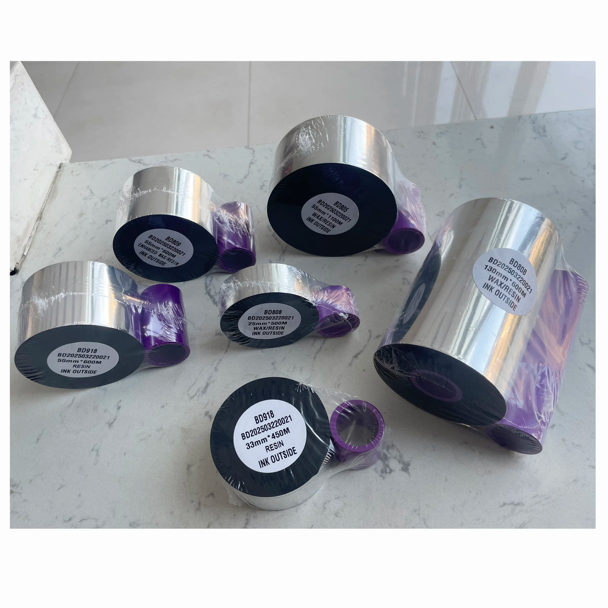Assorted wax/resin ink ribbon rolls with black labels and silver outer wraps in a set