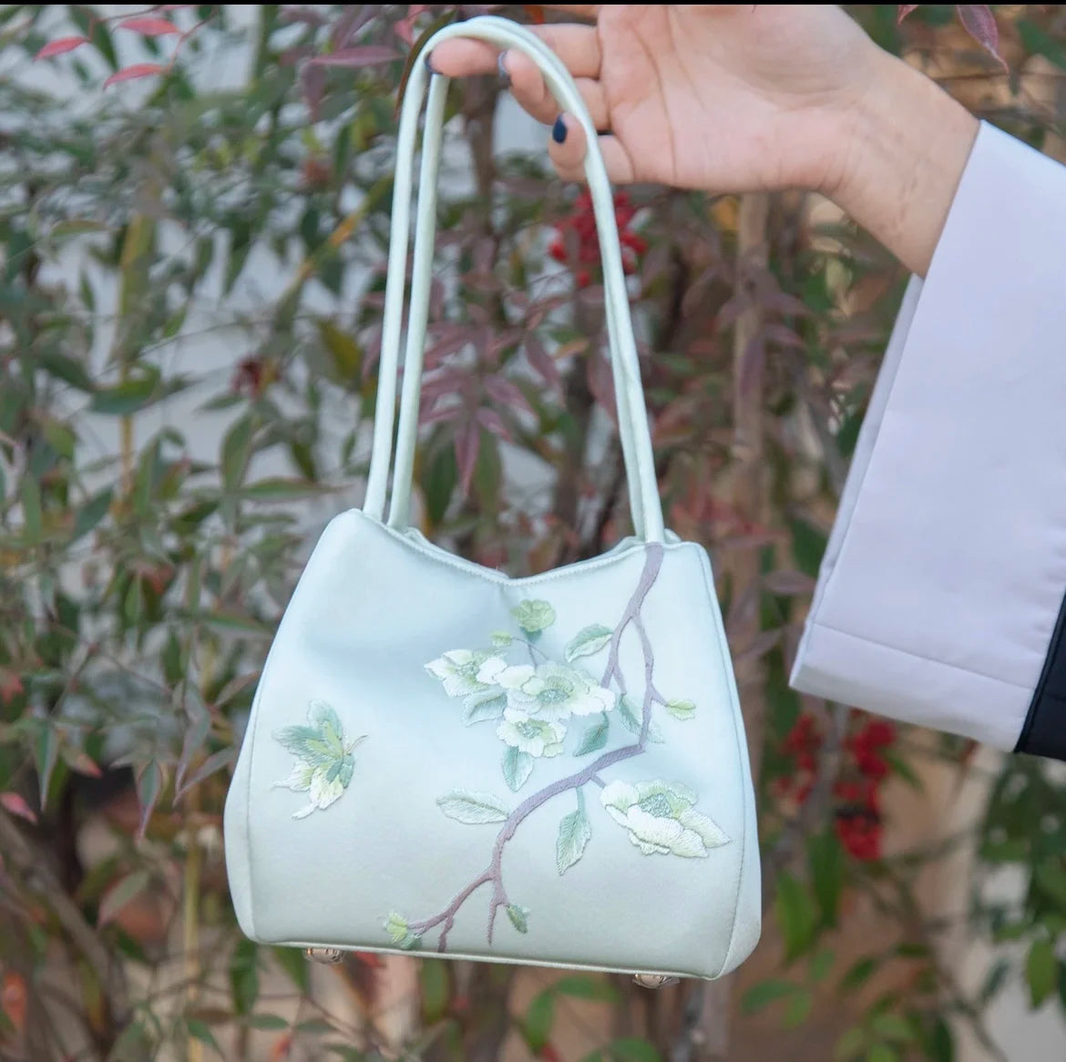 Mint green silk handbag featuring intricate white floral Su embroidery, slender shoulder straps, and a structured base.