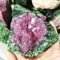 Large rough red and green quartz stone with speckled white patches, held in hand